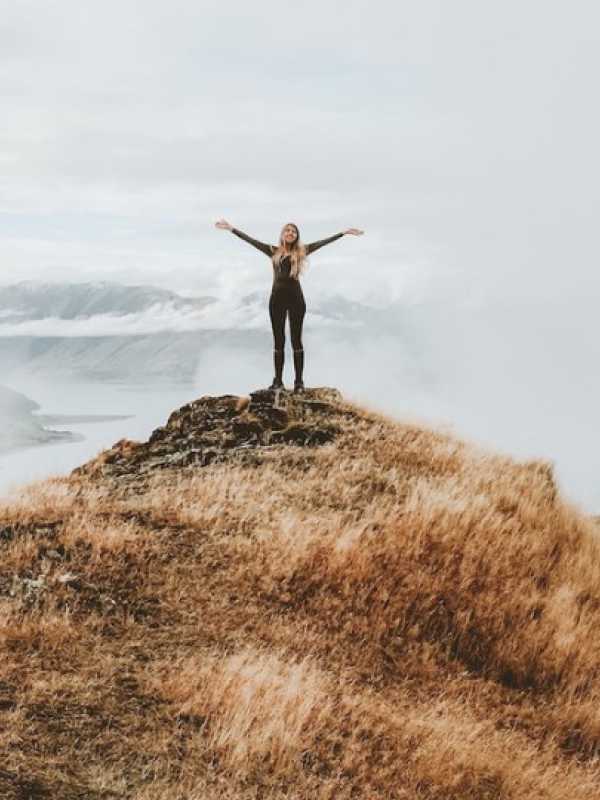 Une femme avec les bras en croix au sommet d'une montagne.