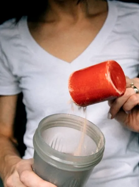 Femme qui met un tasse de protéines dans un malaxeur