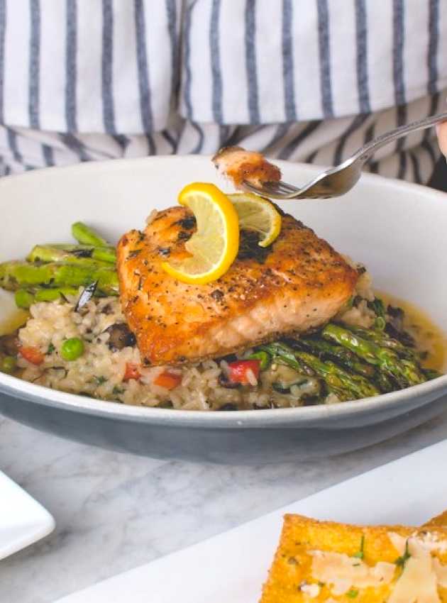 Femme qui mange du saumon sur lit d'asperges et riz aux légumes