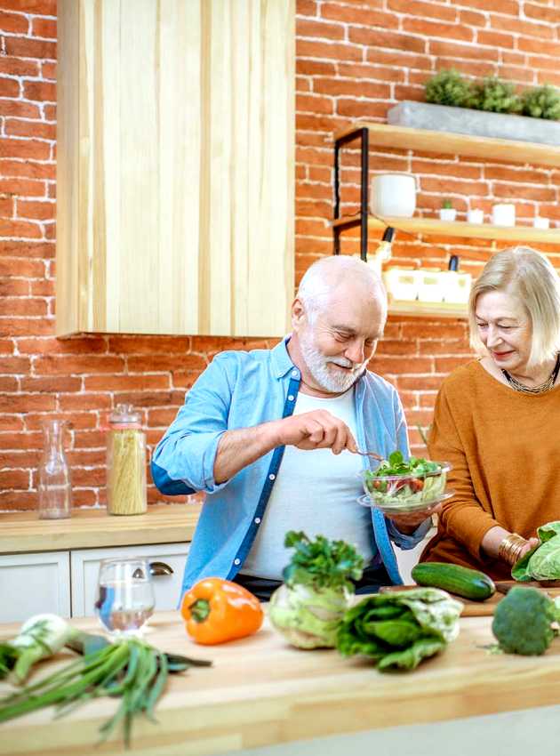 Deux jeunes femmes discutent lors d'une consultation en nutrition, assises à une table blanche dans une cuisine lumineuse. L'une d'elles explique avec des gestes, tandis que l'autre écoute attentivement.